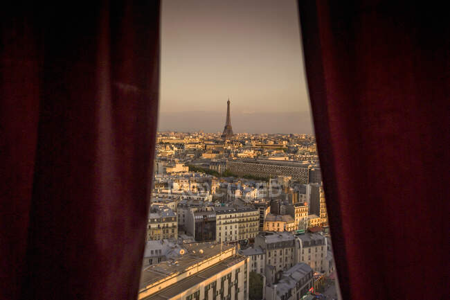 Vista de la ventana de cortina roja del paisaje urbano con la lejana Torre Eiffel - foto de stock