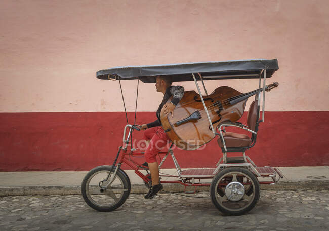 Hombre llevando contrabajo en triciclo en calle colonial, Trinida - foto de stock