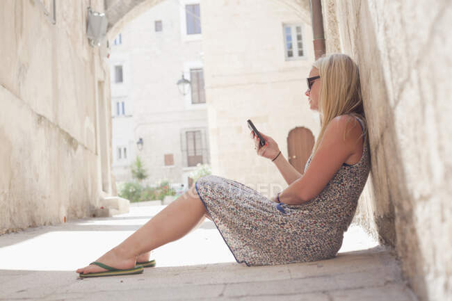 Mujer sentada en el suelo usando teléfono móvil, Monopoli, Puglia, Ita - foto de stock