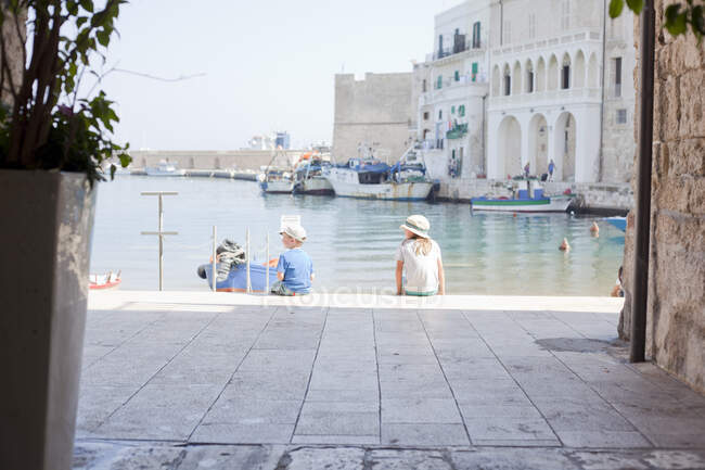 Niño y niña sentados en el puerto, Monopoli, Puglia, Italia - foto de stock