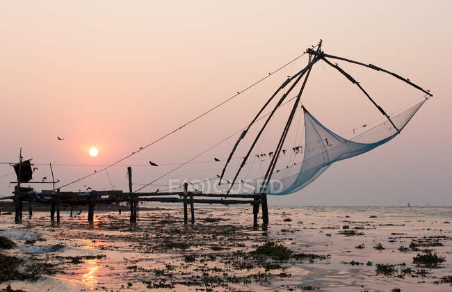 Muelle y redes de pesca en la playa al atardecer, Kochi, Kerala, India - foto de stock