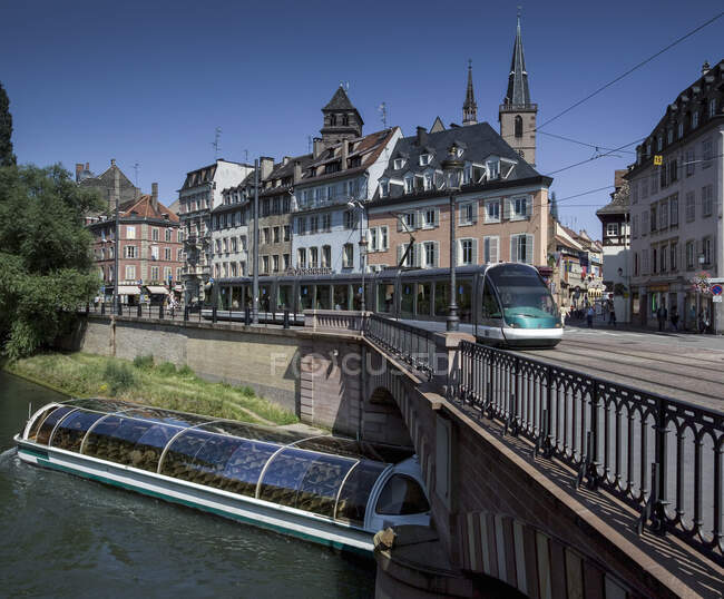 Canal boat tour passing under tram on bridge, Estrasburgo, Francia - foto de stock
