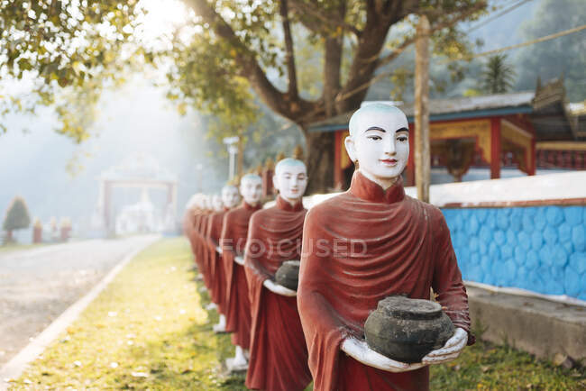 Fila de estatuas monje budista que tienen murciélagos prohibidos, Kaw Ka Thawng Cav - foto de stock