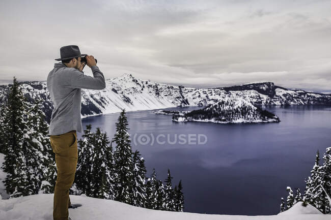 Mann blickt durch Ferngläser auf Crater Lake im Schnee, Oregon, U — Stockfoto