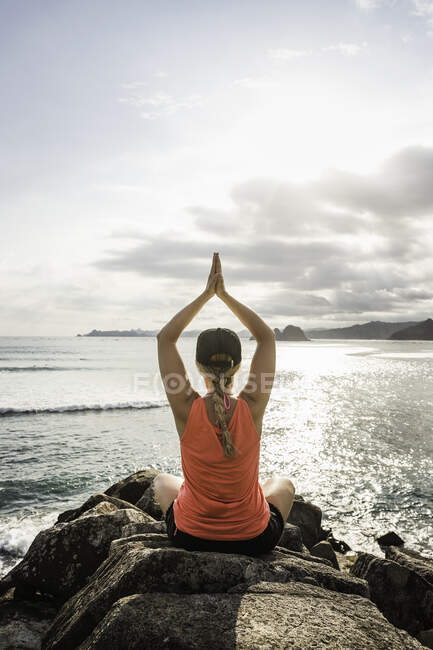 Turismo practicando yoga sobre rocas, Playa Mawi, Lombok, Indonesia - foto de stock