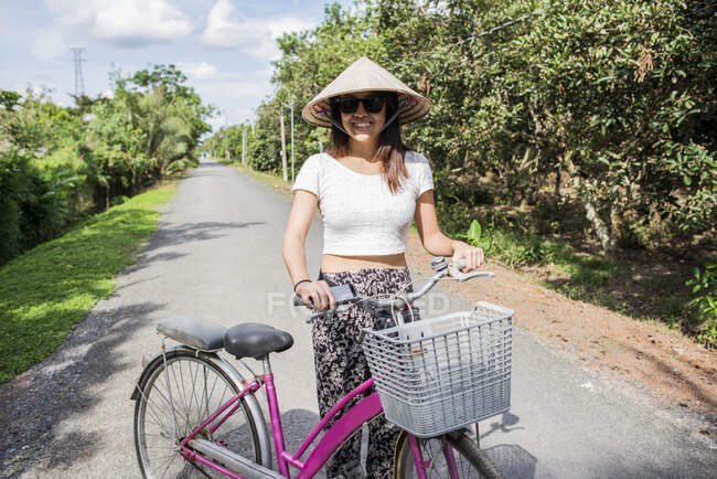 Femme portant un chapeau de riz traditionnel à côté du vélo, Tan Phong Isl — Photo de stock
