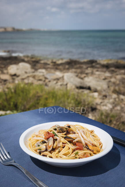 Cuenco de pasta de mariscos en la mesa del restaurante en la costa, Puglia, Ital - foto de stock