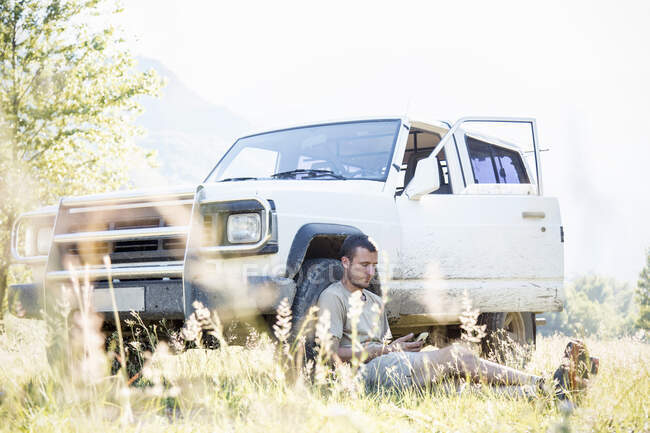 Homem que usa o telemóvel enquanto se inclina contra o pneu do veículo — Fotografia de Stock