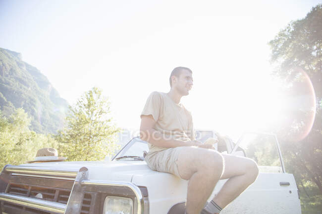 Uomo seduto sul cofano del veicolo, utilizzando il cellulare — Foto stock
