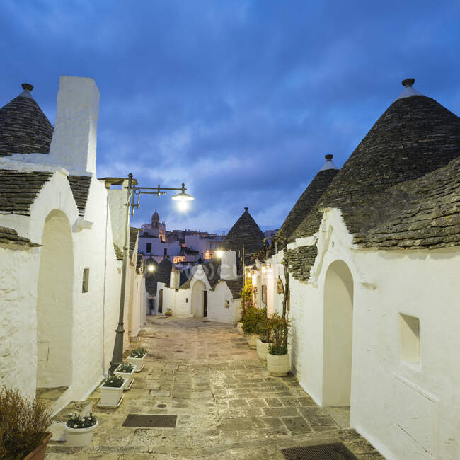 Paved alley and whitewashed trullo houses at dusk, Alberobello, — Stock Photo