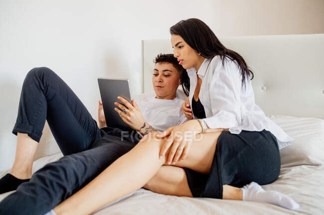 Jovem casal lésbico deitado na cama, olhando para tablet digital. — Fotografia de Stock