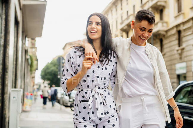 Joven pareja lesbiana caminando brazo en brazo por una calle. - foto de stock