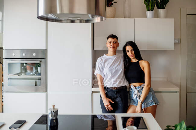 Молода пара лесбіянок стоїть на кухні, дивлячись на камеру . — стокове фото