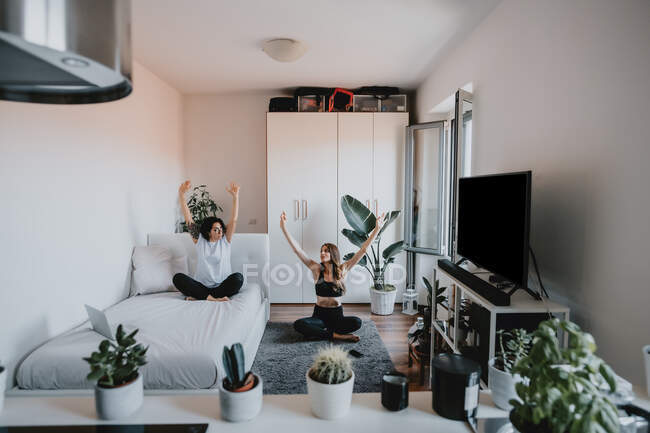 Deux femmes aux cheveux bruns assis dans un appartement, faisant du yoga. — Photo de stock
