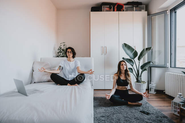 Zwei Frauen mit braunen Haaren sitzen in einer Wohnung und meditieren. — Stockfoto