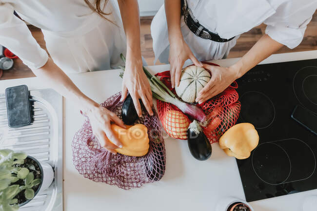 Angle élevé gros plan de deux femmes debout dans une cuisine, enlever les légumes du filet de magasinage. — Photo de stock