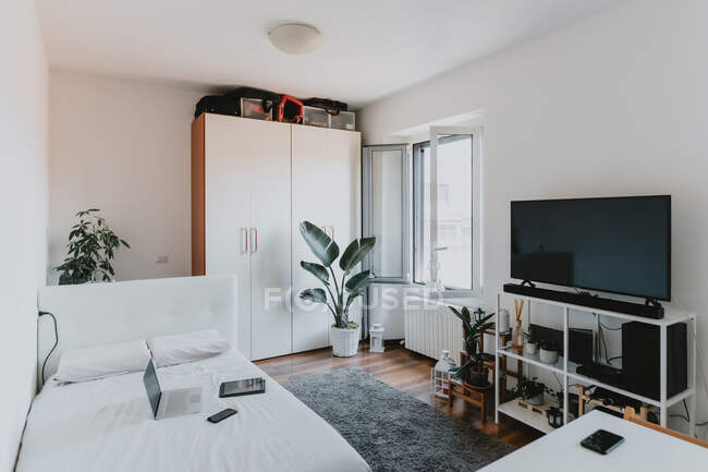 Vista interna del soggiorno con pavimento in legno, divano letto bianco e TV a schermo piatto su scaffale bianco. — Foto stock