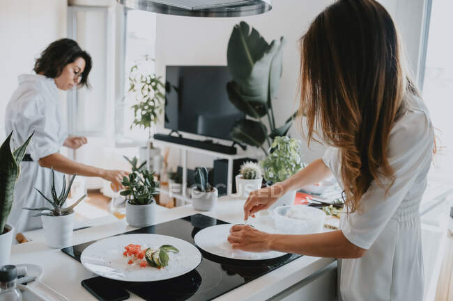 Две улыбающиеся женщины с каштановыми волосами стоят на кухне и готовят еду.. — стоковое фото