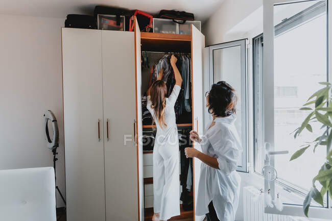 Дві жінки з коричневим волоссям, що стоять в квартирі, вішають одяг в шафі . — стокове фото