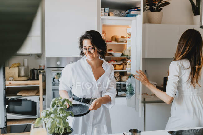 Two smiling women with brown hair standing in a kitchen, preparing food. — Stock Photo