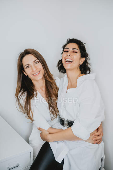 Портрет двух улыбающихся женщин с каштановыми волосами, обнимающихся, смотрящих в камеру. — стоковое фото