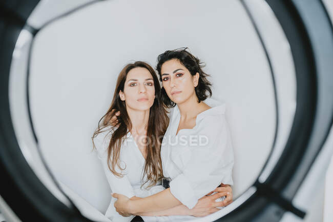 Portrait of two smiling women with brown hair embracing, looking at camera. — Stock Photo