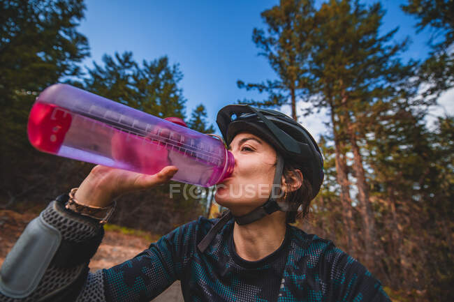 Mujer ciclista de montaña bebiendo de la botella de agua en un bosque en - foto de stock