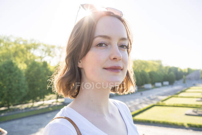 Portrait of young woman with brunette hair standing in a park, smiling at camera. — Stock Photo