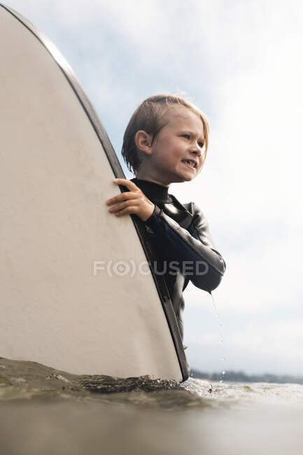 Портрет мальчика в мокром костюме, несущего доску для серфинга в океан, Санта-Барбара, Калифорния, США. — стоковое фото