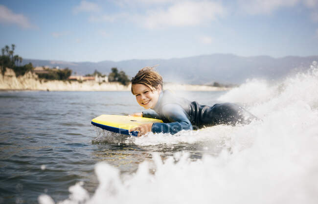 Ritratto di giovane ragazzo in muta, sdraiato su tavola da surf, onda d'equitazione, Santa Barbara, California, USA. — Foto stock