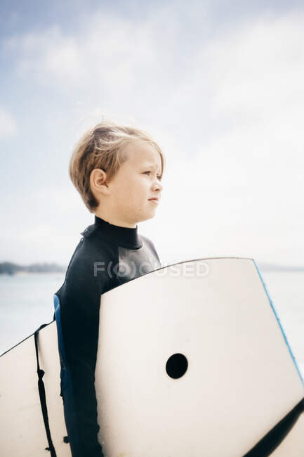 Portrait of young boy wearing wet suit, carrying surfboard into ocean, Santa Barbara, California, USA. — Stock Photo