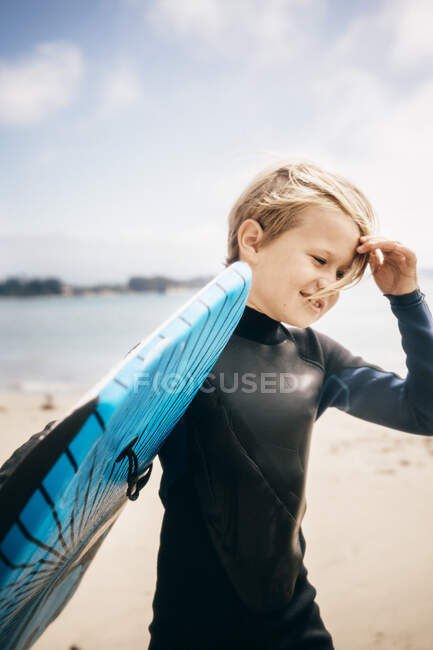 Porträt eines kleinen Jungen im Neoprenanzug, der Surfbretter ins Meer trägt, Santa Barbara, Kalifornien, USA. — Stockfoto