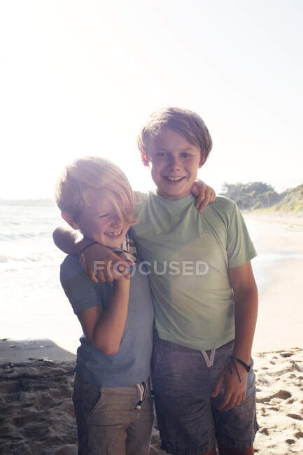 Portrait of two smiling boys, standing on beach, arm around shoulder, looking at camera, Santa Barbara, California, USA. — Stock Photo