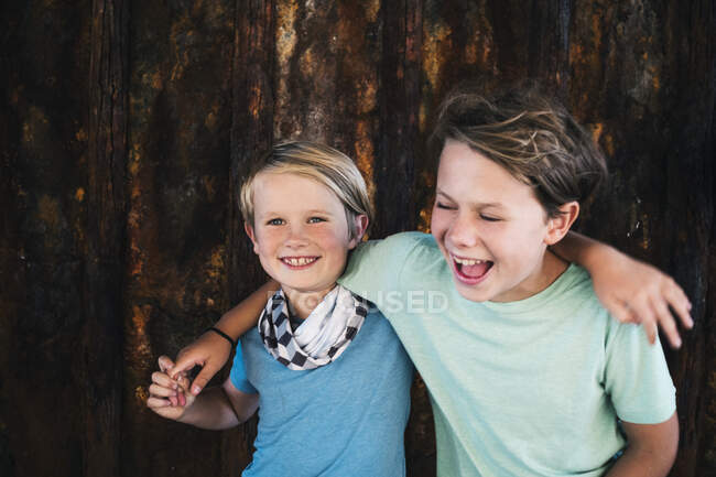 Retrato de dos chicos sonrientes, brazo alrededor del hombro, mirando a la cámara. - foto de stock