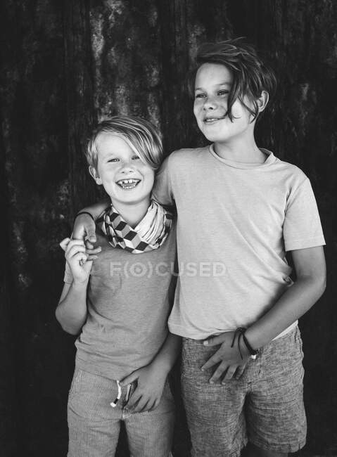 Retrato de dos chicos sonrientes, brazo alrededor del hombro, mirando a la cámara. - foto de stock