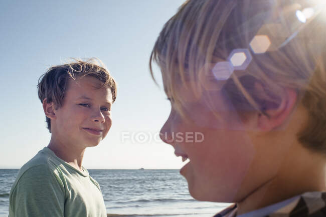 Retrato de la cabeza y los hombros de dos chicos sonrientes junto al océano. - foto de stock