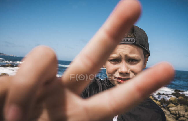 Garçon debout près de l'océan près de Carmel, Californie, États-Unis, faisant signe de victoire, regardant la caméra. — Photo de stock