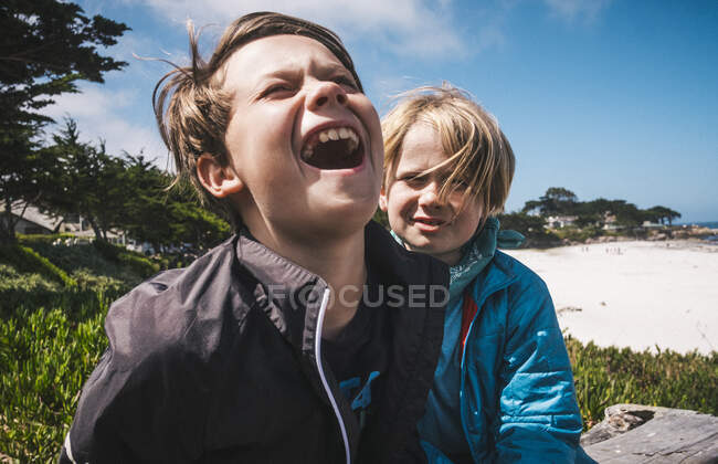Zwei Jungen sitzen am Sandstrand in der Nähe von Carmel, Kalifornien, USA und necken sich. — Stockfoto