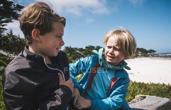 Dois meninos sentados na praia perto de Carmel, Califórnia, EUA, provocando uns aos outros. — Fotografia de Stock
