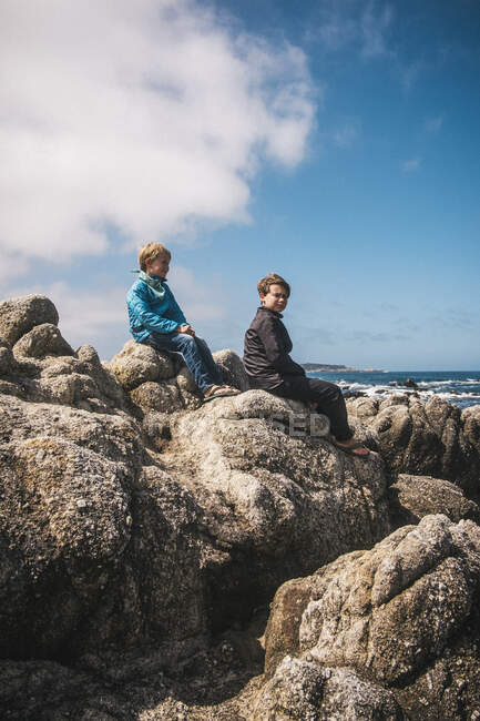 Dois meninos sentados em rochas junto ao oceano perto de Carmel, Califórnia, EUA. — Fotografia de Stock