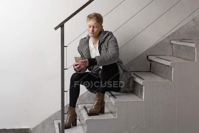 Женщина сидит на лестнице, проверяет мобильный телефон — стоковое фото