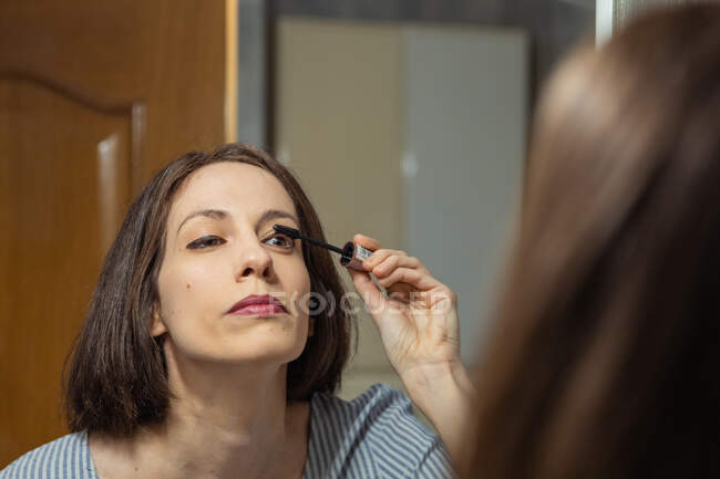 Женщина стоит перед зеркалом, наносит макияж — стоковое фото