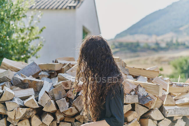 Mujer joven con el pelo largo, por pila de troncos, vista lateral - foto de stock