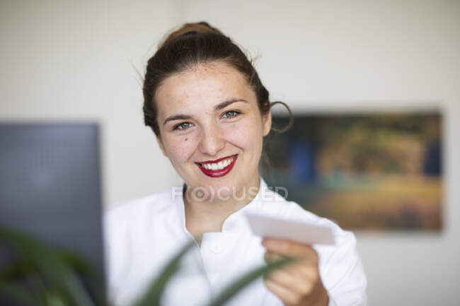 Young woman at computer, handing over card — Stock Photo