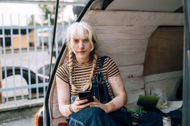 Junge Frau sitzt mit Handy im hinteren Teil des Transporters — Stockfoto