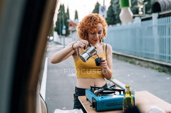 Jovem mulher fazendo café na parte de trás da van — Fotografia de Stock