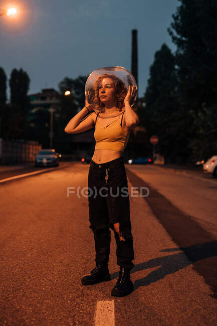 Giovane donna in piedi sulla strada con ciotola di vetro sulla testa — Foto stock