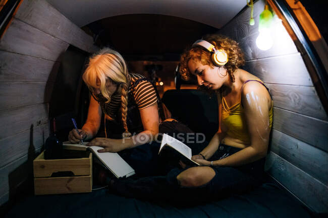Молоді жінки читають і роблять нотатки позаду фургона — стокове фото