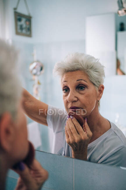 Seniorin blickt in Spiegel und schminkt sich — Stockfoto