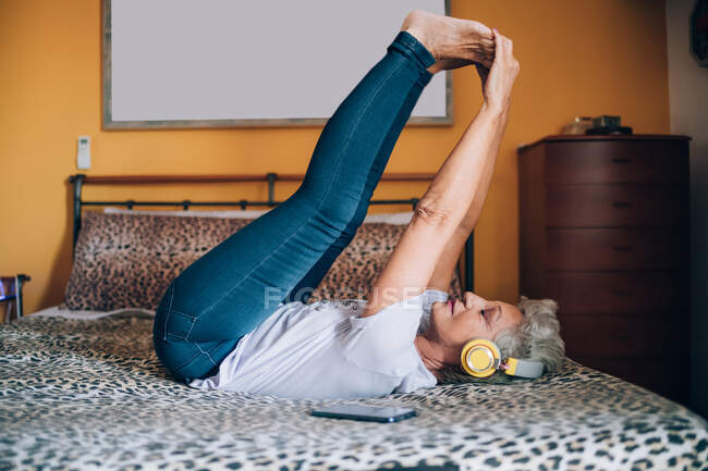 Woman stretching on bed, listening to headphones — Stock Photo